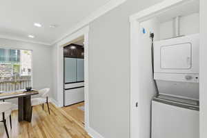 Laundry area featuring crown molding, stacked washer / drying machine, light wood finished floors, and recessed lighting