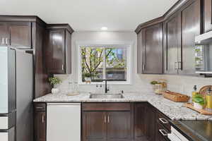 Kitchen with freestanding refrigerator, dark wood finish cabinets, and dishwasher