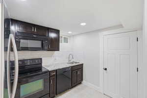 Kitchen featuring dark wood finish cabinets, black appliances, light stone counters, backsplash, and light tile patterned flooring