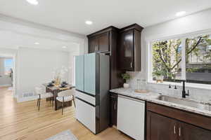 Kitchen featuring dark wood finish cabinets, light stone countertops, white dishwasher, freestanding refrigerator, and decorative backsplash