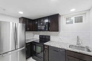 Kitchen with black appliances, dark wood finish cabinetry, light stone countertops, backsplash, and recessed lighting
