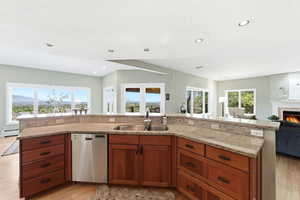 Kitchen featuring open floor plan, wood finish cabinets, stainless steel dishwasher, light wood-style floors, and a glass covered fireplace