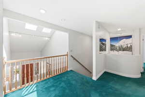 Hall with lofted ceiling, carpet flooring, track lighting, an upstairs landing, and a skylight