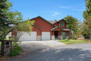 Craftsman-style home with driveway, stone siding, a chimney, a garage, and a front lawn