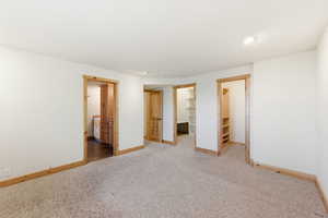 Unfurnished bedroom with a spacious closet, ensuite bath, light colored carpet, and recessed lighting