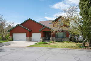 View of front of home featuring stone siding, concrete driveway, a front lawn, and an attached garage