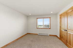 Unfurnished bedroom featuring light carpet, a baseboard radiator, a closet, and recessed lighting