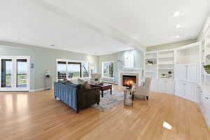 Living room featuring a fireplace with flush hearth, light wood-style floors, recessed lighting, a baseboard heating unit, and built in shelves