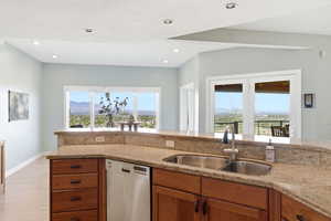 Kitchen with light stone counters, dishwasher, wood finish cabinets, light wood-style flooring, and lofted ceiling