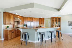 Kitchen with a breakfast bar area, wood finish cabinets, exhaust hood, stainless steel appliances, and recessed lighting