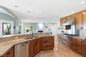 Kitchen featuring stainless steel appliances, a fireplace, wood finish cabinets, ventilation hood, and recessed lighting