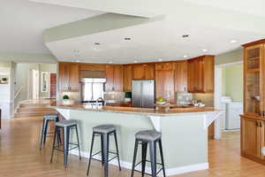 Kitchen with a breakfast bar area, decorative backsplash, light wood-type flooring, high quality fridge, and recessed lighting
