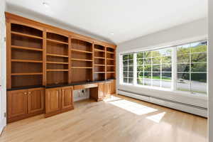 Unfurnished office with built in desk, baseboard heating, and light wood-style floors