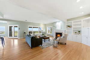 Living room with recessed lighting, light wood-type flooring, a glass covered fireplace, a baseboard heating unit, and french doors