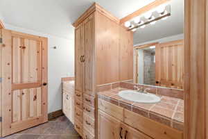 Full bathroom featuring two vanities, stone tile floors, and tiled shower