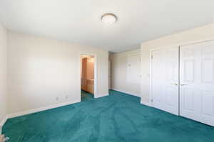 Unfurnished bedroom featuring ensuite bath, dark carpet, and a closet
