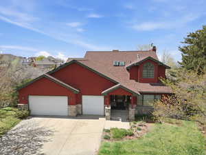 View of front of home with stone siding, an attached garage, driveway, a shingled roof, and a chimney
