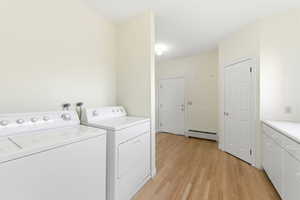 Laundry room featuring light wood-type flooring, washing machine and clothes dryer, and a baseboard radiator