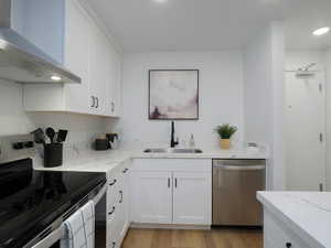 Kitchen featuring stainless steel appliances, white cabinetry, light wood finished floors, light stone countertops, and recessed lighting
