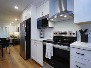Kitchen featuring stainless steel appliances, white cabinetry, light stone counters, light wood-style flooring, and recessed lighting