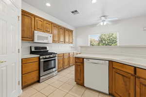 Kitchen with wood finish cabinets, white appliances, light countertops, a ceiling fan, and light tile patterned floors