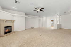 Unfurnished living room with a ceiling fan, a tiled fireplace, light colored carpet, and recessed lighting