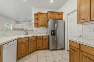 Kitchen featuring stainless steel fridge with ice dispenser, dishwasher, light countertops, wood finish cabinets, and light tile patterned flooring