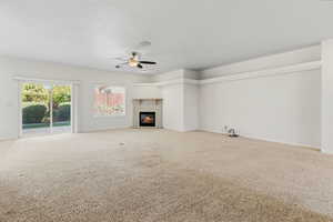 Unfurnished living room featuring a ceiling fan, carpet flooring, and a glass covered fireplace