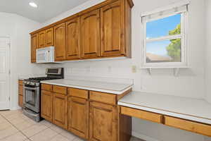 Kitchen featuring stainless steel gas stove, light countertops, wood finish cabinetry, white microwave, and light tile patterned floors