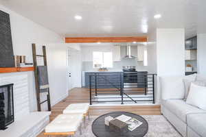 Living room with light wood finished floors, a stone fireplace, recessed lighting, and beam ceiling