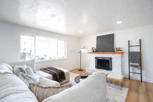 Living room with light wood finished floors, a fireplace with raised hearth, a textured ceiling, and recessed lighting