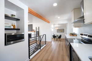 Kitchen with stainless steel appliances, light wood finished floors, recessed lighting, light stone counters, and beam ceiling