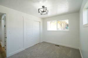 Unfurnished bedroom featuring a textured ceiling, carpet flooring, a closet, and suspended lighting