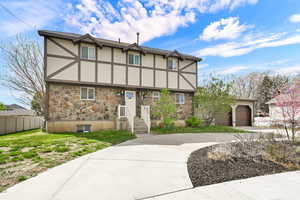 Tudor-style house featuring stone siding, stucco siding, and driveway