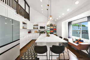 Kitchen with stainless steel appliances, vaulted ceiling, white cabinetry, a kitchen bar, and dark wood-type flooring
