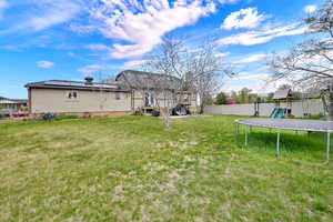 Rear view of house with a trampoline, a fenced backyard, a playground, stucco siding, and roof mounted solar panels