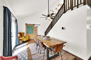 Dining room featuring a barn door, wood finished floors, lofted ceiling, and ceiling fan