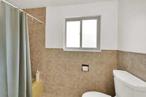 Bathroom featuring shower / bath combination with curtain, tile walls, and wainscoting
