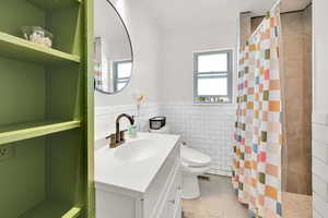 Bathroom with tile walls, vanity, a shower stall, a wainscoted wall, and light tile patterned flooring