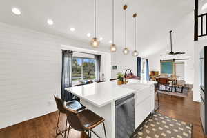 Kitchen featuring a kitchen breakfast bar, a kitchen island with sink, white cabinets, pendant lighting, and stainless steel dishwasher