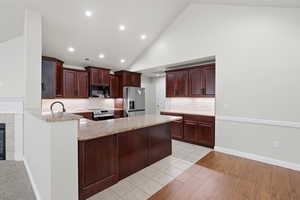 Kitchen with a peninsula, lofted ceiling, tasteful backsplash, stainless steel appliances, and light stone countertops