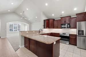 Kitchen with a peninsula, stainless steel appliances, light stone countertops, vaulted ceiling, and light colored carpet