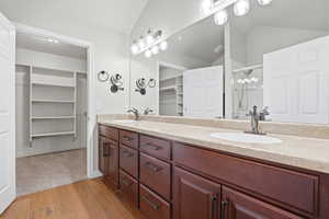 Primary bathroom featuring a spacious closet, double vanity, a shower stall, vaulted ceiling, and light wood-style floors
