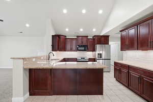 Kitchen featuring a peninsula, decorative backsplash, light stone countertops, lofted ceiling, and recessed lighting