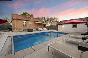Pool at dusk with an outdoor lounge area, a patio area, and a fenced backyard