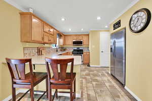 Kitchen featuring a kitchen breakfast bar, a peninsula, stainless steel appliances, ornamental molding, and inlaid floor details