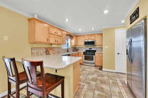 Kitchen featuring a peninsula, stainless steel appliances, a breakfast bar, light wood finish cabinets, and ornamental molding