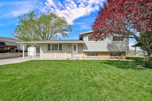 Tri-level home with brick siding, a front yard, an attached carport, a storage unit, and concrete driveway
