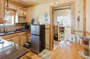 Kitchen featuring light wood-style flooring, freestanding refrigerator, dark stone countertops, light wood finish cabinets, and wooden walls