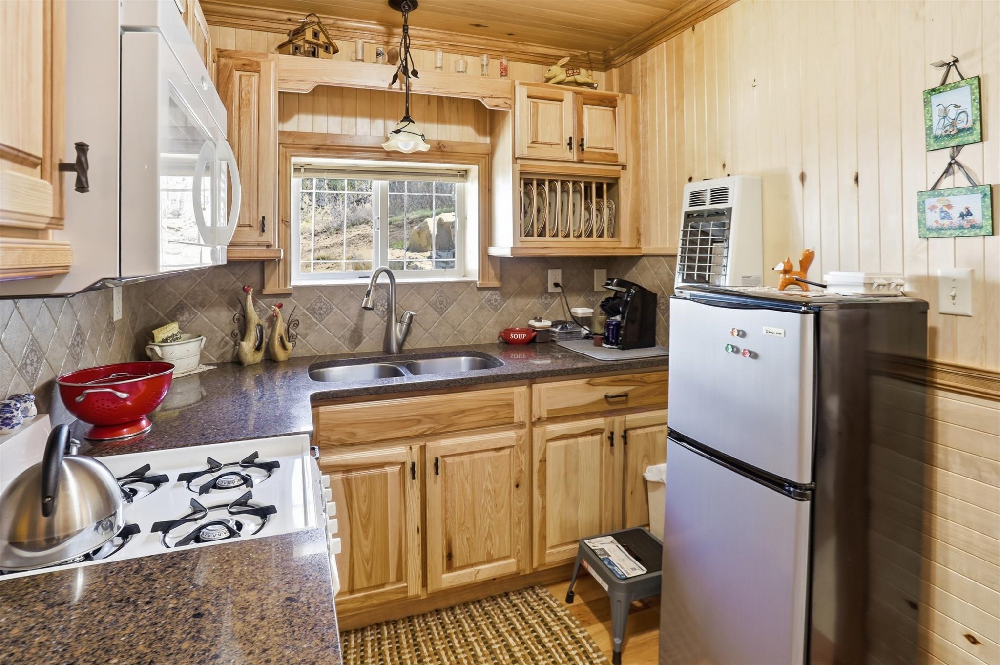 Kitchen featuring white appliances, hanging light fixtures, light wood finish cabinetry, dark stone countertops, and wood walls